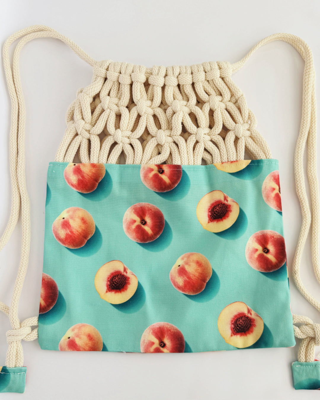 Handmade macramé backpack with cream macramé top and turquoise bottom featuring a peach fruit print – Tropica Nero design, tropical and light in style.