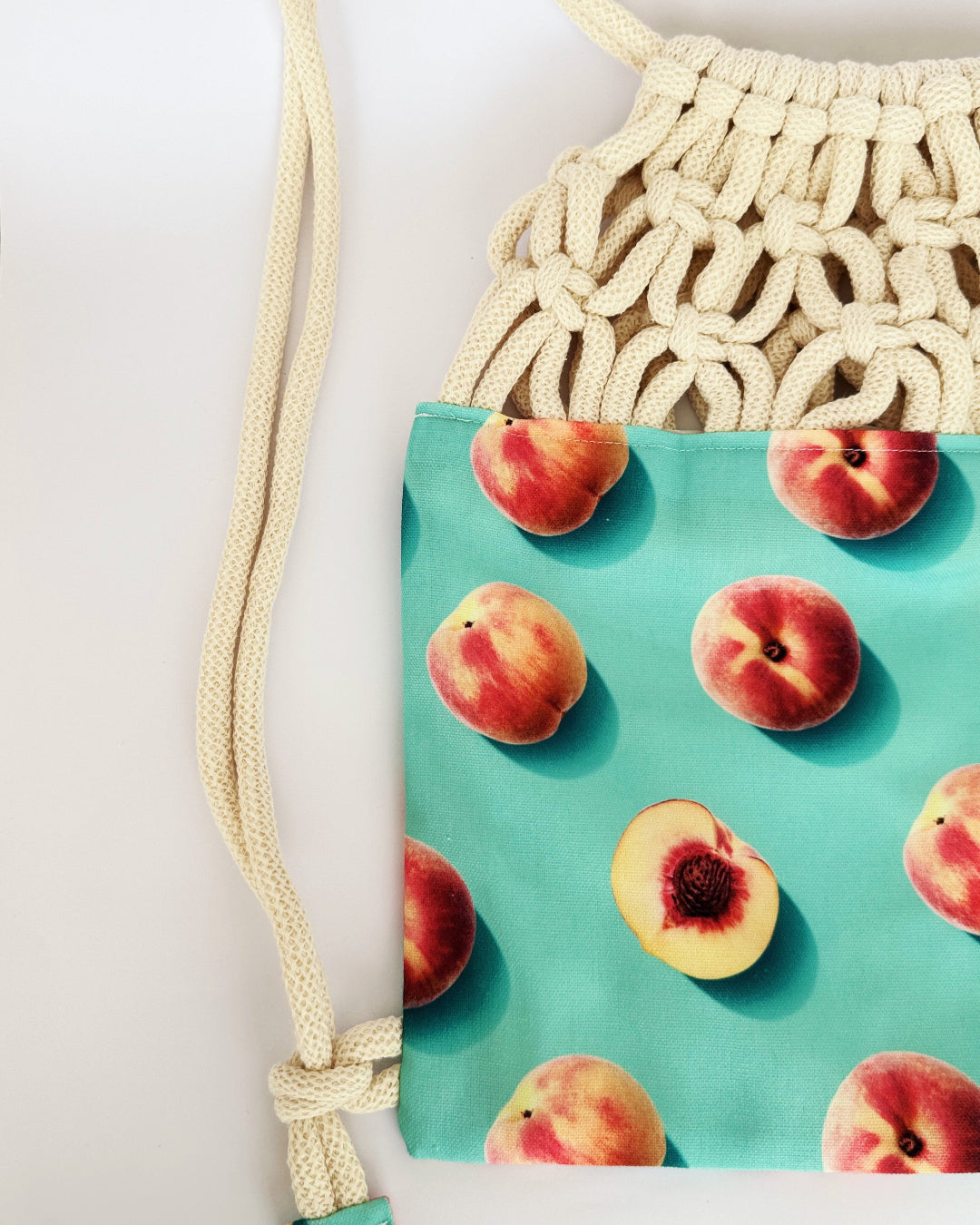 Handmade macramé backpack with cream macramé top and turquoise bottom featuring a peach fruit print – Tropica Nero design, tropical and light in style.