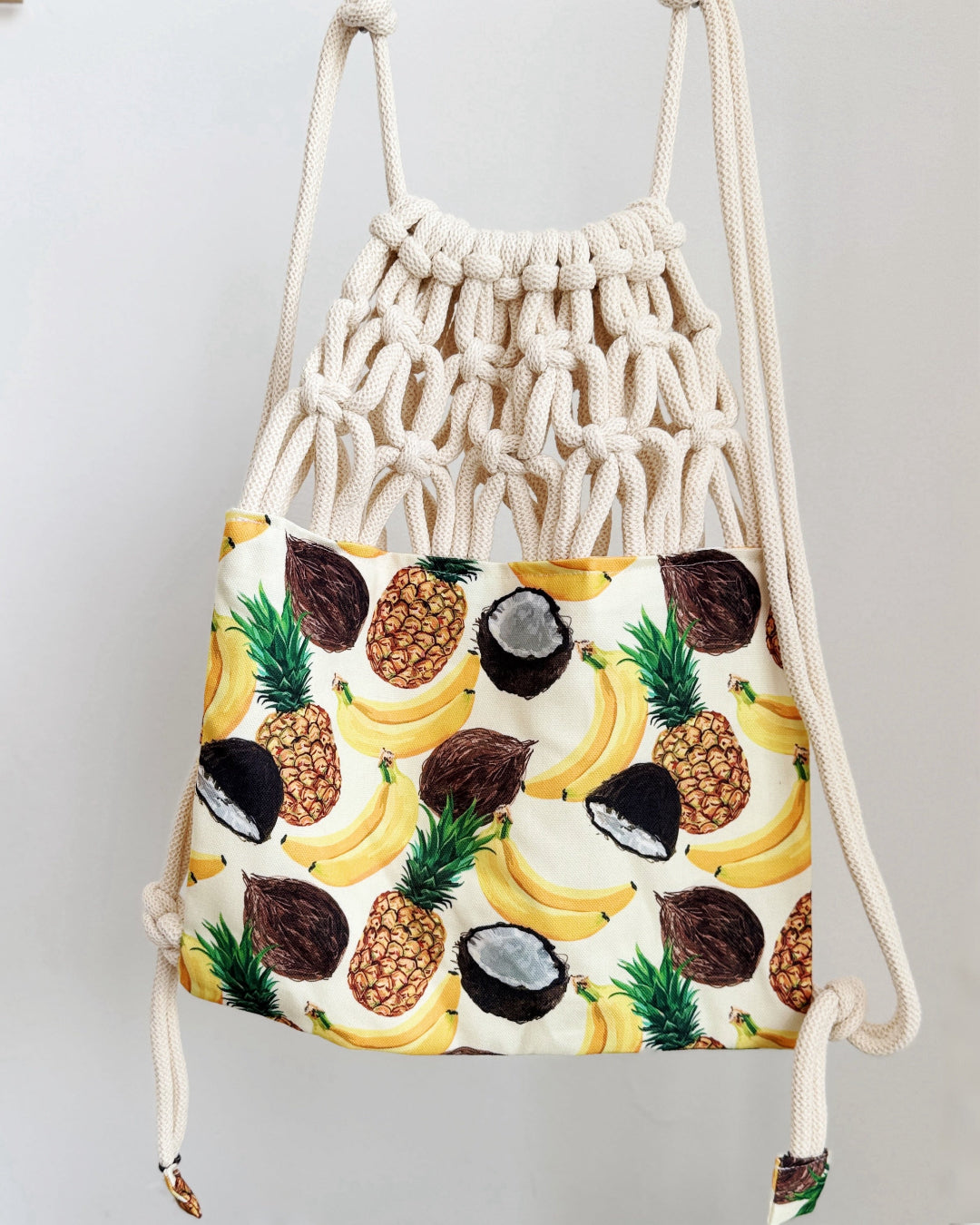 Handmade macramé backpack with soft cream macramé top and tropical fruit print canvas bottom in beige tones – Tropica Zanzibar design.