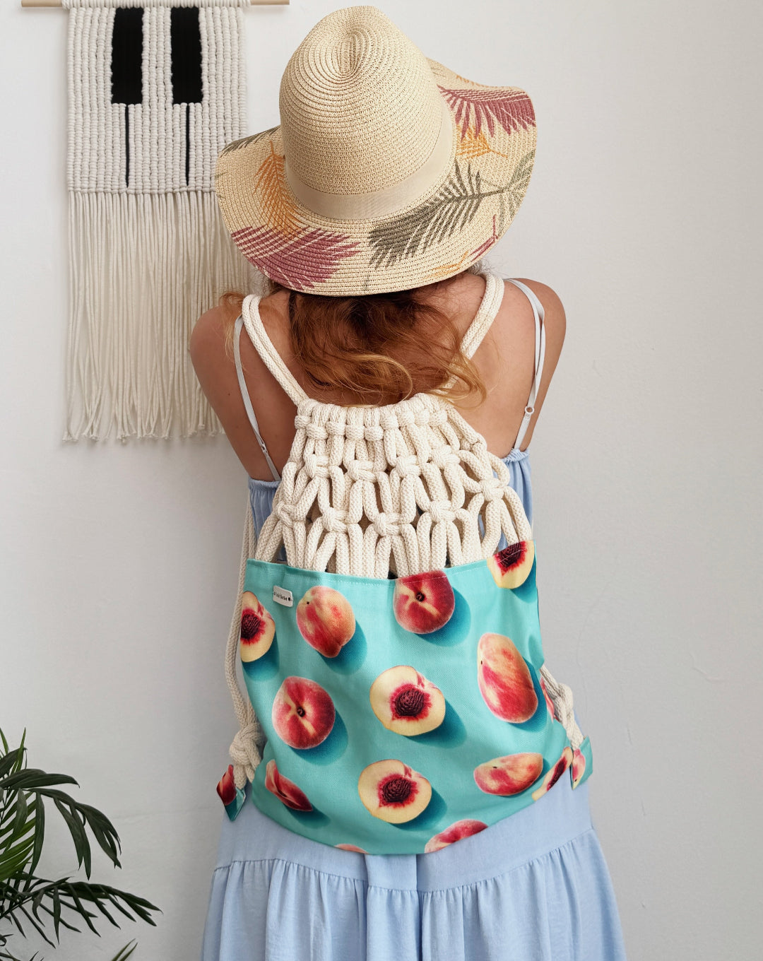Handmade macramé backpack with cream macramé top and turquoise bottom featuring a peach fruit print – Tropica Nero design, tropical and light in style. on a model.