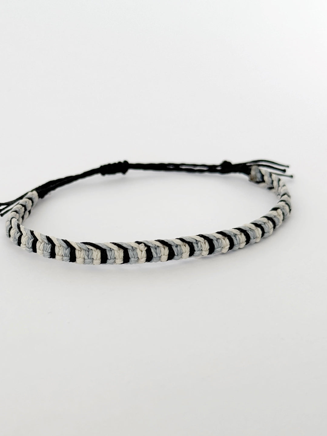 צמיד Tide מקרמה לגבר בעבודת יד על רקע בהיר, בגווני שחור ותכלת-אפרפר.