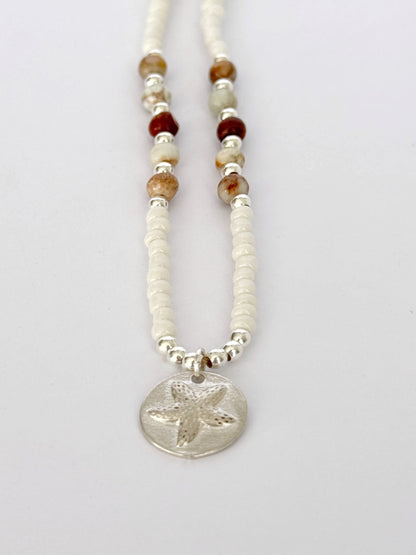 שרשרת Mirage היא שרשרת חרוזים עדינה בעבודת יד, בגוונים חמים של לבן, קרם ואדמדם. השילוב בין החרוזים הקטנים לבין אלמנט הכסף יוצר מראה רגוע ונקי, כזה שמרגיש כמו קו של אור על חול חם.