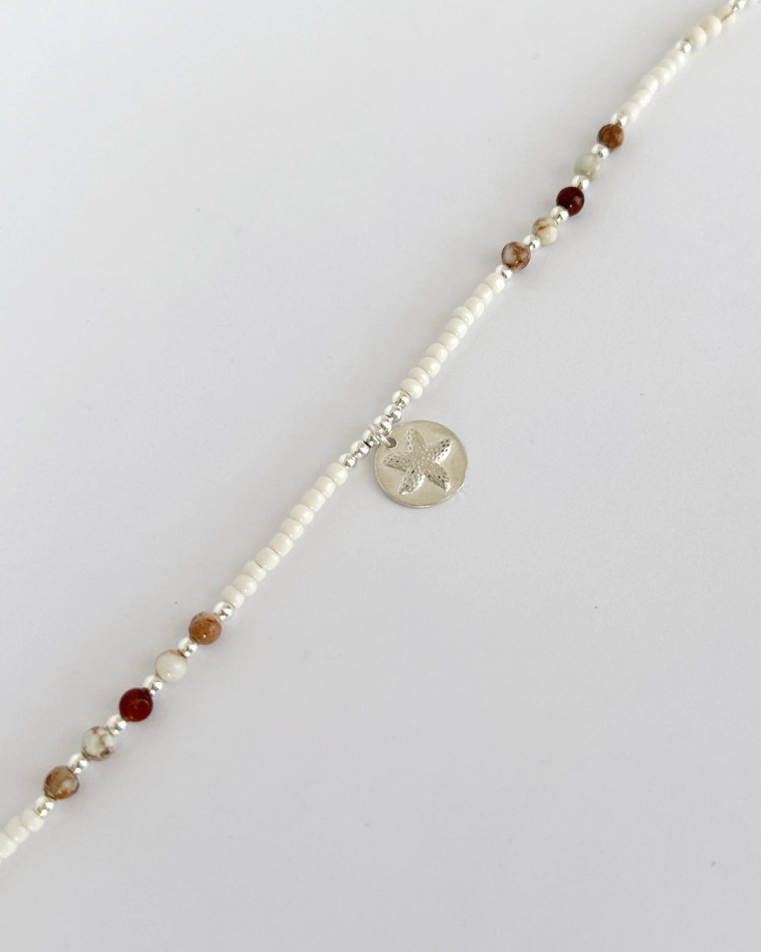 שרשרת Mirage היא שרשרת חרוזים עדינה בעבודת יד, בגוונים חמים של לבן, קרם ואדמדם. השילוב בין החרוזים הקטנים לבין אלמנט הכסף יוצר מראה רגוע ונקי, כזה שמרגיש כמו קו של אור על חול חם.