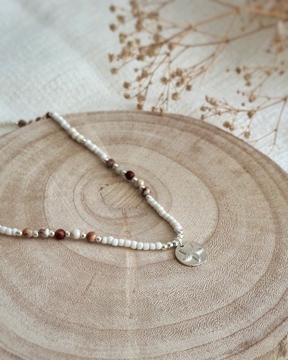 שרשרת Mirage היא שרשרת חרוזים עדינה בעבודת יד, בגוונים חמים של לבן, קרם ואדמדם. השילוב בין החרוזים הקטנים לבין אלמנט הכסף יוצר מראה רגוע ונקי, כזה שמרגיש כמו קו של אור על חול חם.