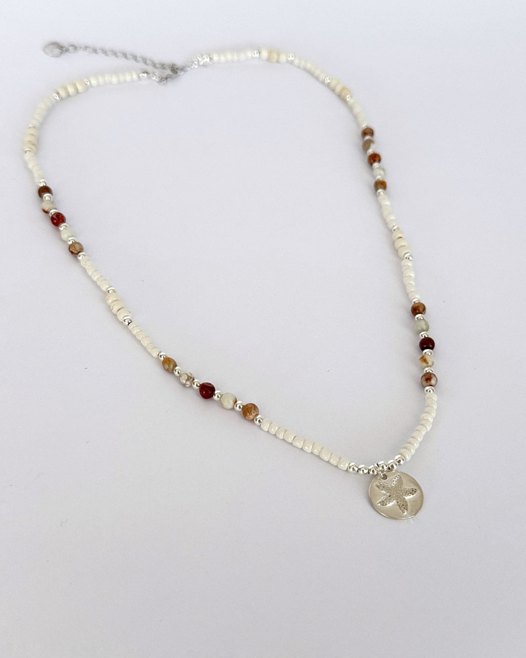 שרשרת Mirage היא שרשרת חרוזים עדינה בעבודת יד, בגוונים חמים של לבן, קרם ואדמדם. השילוב בין החרוזים הקטנים לבין אלמנט הכסף יוצר מראה רגוע ונקי, כזה שמרגיש כמו קו של אור על חול חם.