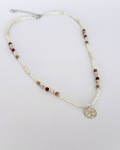 שרשרת Mirage היא שרשרת חרוזים עדינה בעבודת יד, בגוונים חמים של לבן, קרם ואדמדם. השילוב בין החרוזים הקטנים לבין אלמנט הכסף יוצר מראה רגוע ונקי, כזה שמרגיש כמו קו של אור על חול חם.