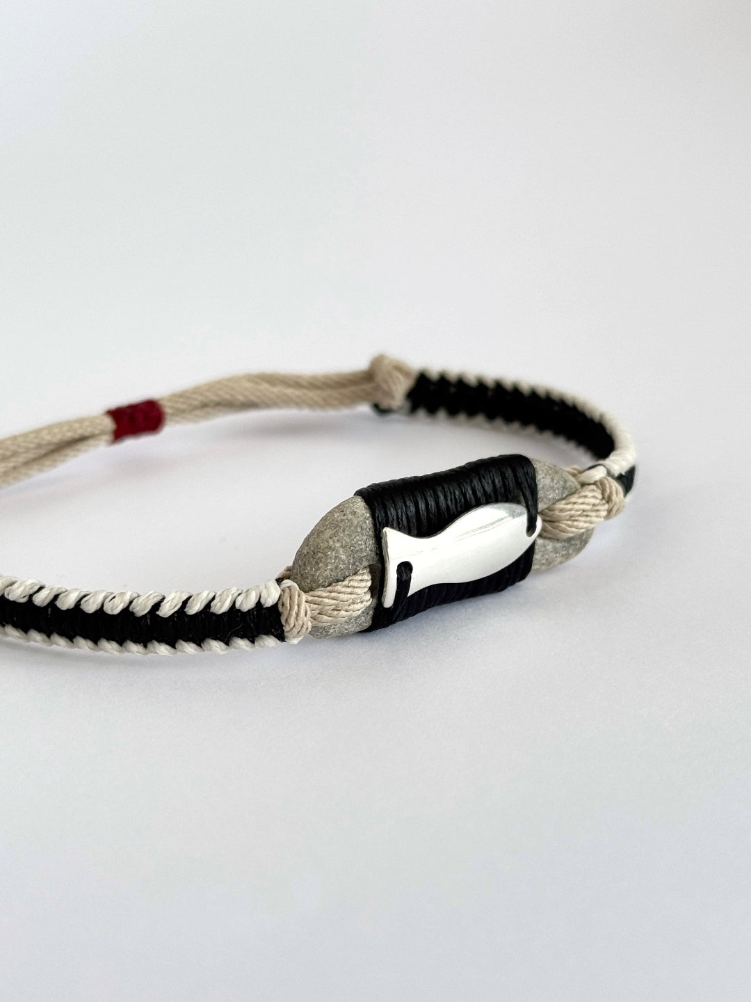 Close-up of natural pebble and silver fish pendant in handmade macramé bracelet