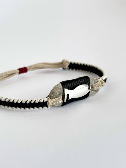 Close-up of natural pebble and silver fish pendant in handmade macramé bracelet