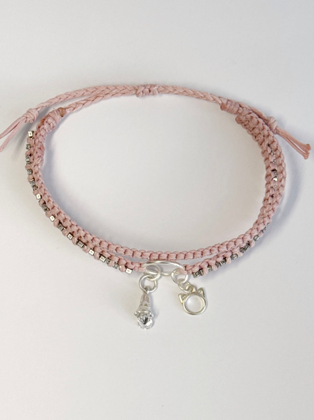 צמיד מקרמה כפול בגוון ורוד בייבי עם שרשרת זירקונים שזורה ותליוני כסף של חתול ופעמון - צמיד Stardust של Lala Fshasha.