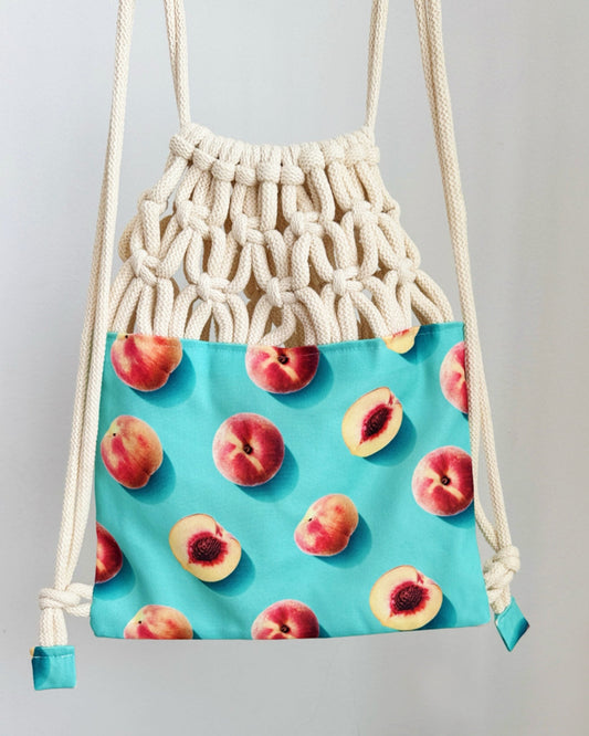 Handmade macramé backpack with cream macramé top and turquoise bottom featuring a peach fruit print – Tropica Nero design, tropical and light in style.